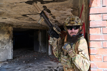 Fototapeta premium Bearded Soldier in Tactical Gear With Rifle Smiling Against Brick Wall in Urban Ruins