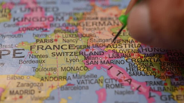 Man Pointing Green Pin on Switzerland Location on Paper World Map Close Up