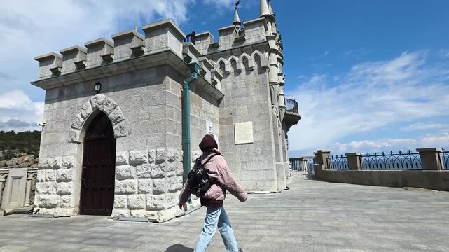 Young woman with a backpack exploring the famous swallow's nest castle, a historic landmark and popular tourist attraction situated on the aurora cliff overlooking the black sea in crimea