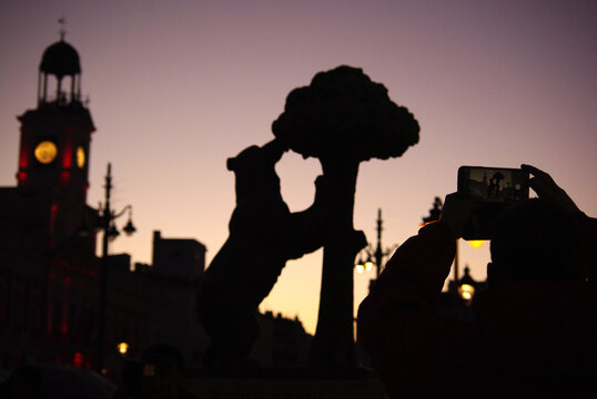 Unas manos y un tel&eacute;fono m&oacute;vil hacen una foto a las siluetas caracter&iacute;sticas de la ciudad de Madrid con la estatua del Oso de Madro&ntilde;o y el reloj de Puerta del Sol. Madrid
