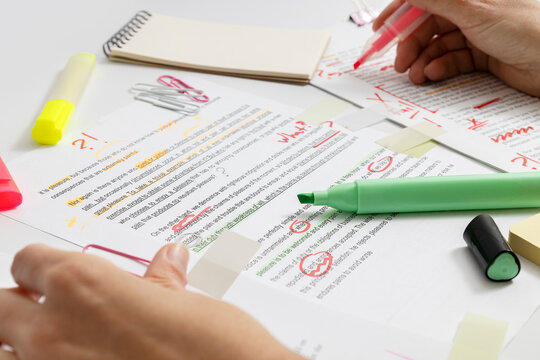 Close-up of proofreading process with red, green pens corrections and highlighted text, editor reviewing document and marking grammar and spelling errors