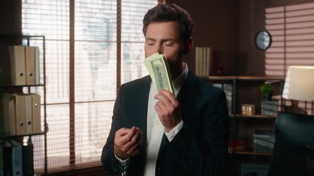 Happy rich Caucasian middle-aged business man holding cash sniffing money smiling looking at camera investing profit at office successful male businessman hold banknotes dollars sniff aroma smile