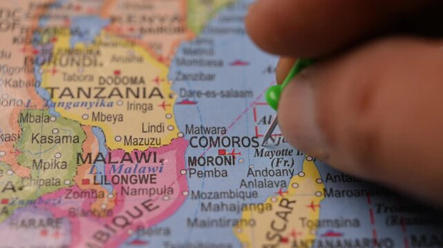 Man Pointing Green Pin on Comoros Location on Paper World Map Close Up
