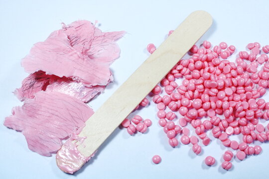 Pink Hard Wax Beans With Wooden Spatula And Used Wax Strips For Hair Removal On White Background