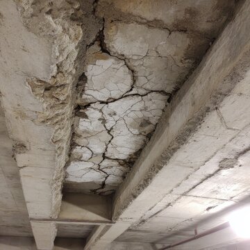 Severely cracked and spalling concrete ceiling showing structural damage and deterioration