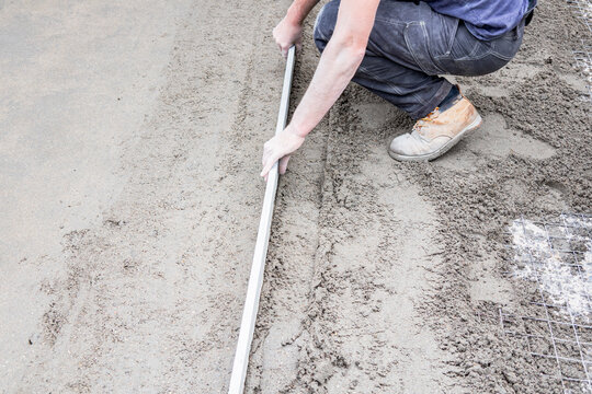 Worker leveling concrete with screed for slab foundation