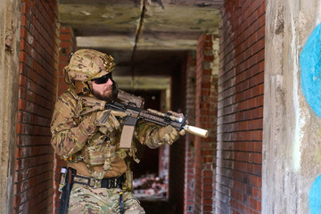Fototapeta premium Tactical Soldier in Camouflage Gear With Rifle Clearing Abandoned Brick Building During Urban Training