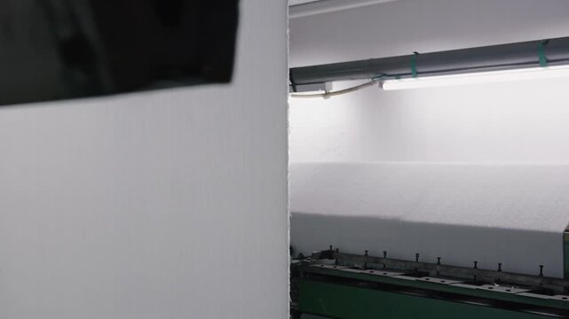 Factory worker controlling an industrial machine processing a large roll of white synthetic material