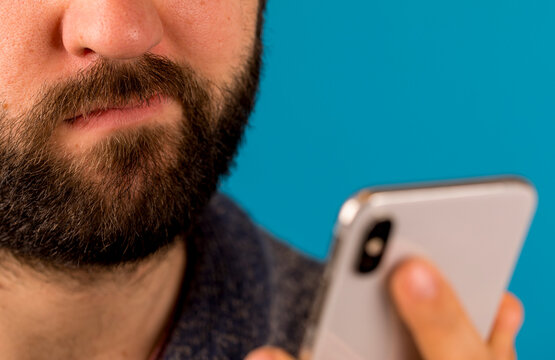 Close up photo of a bearded man focused on his smartphone against a blue background, perfect for tec