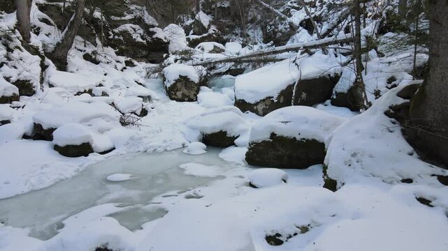 A peaceful and remote winter landscape featuring snow-covered trees, frozen sections of a river, and a winding path marked with many human footprints.