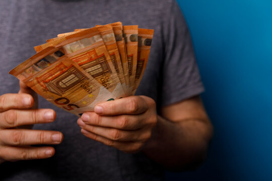 Close-up of a man's hands holding Euro banknotes on a blue backdrop. Perfect for financia
