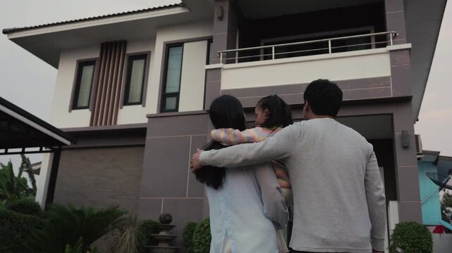 happy family, father and mother holding and hugging with child girl while standing in front of their modern house

