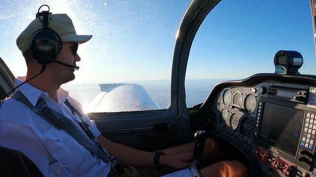 Pilot Flying Small Aircraft Cockpit with Avionics Dashboard and Clear Blue Sky Horizon. Young Male Pilot in Aviation Headset Controls Light Plane Cockpit During Daytime Flight