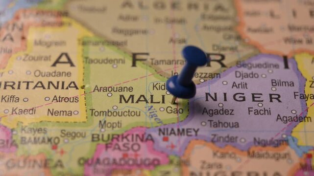 Man Pointing Blue Pin Marking Mali Location on Paper World Map Close Up Travel Concept