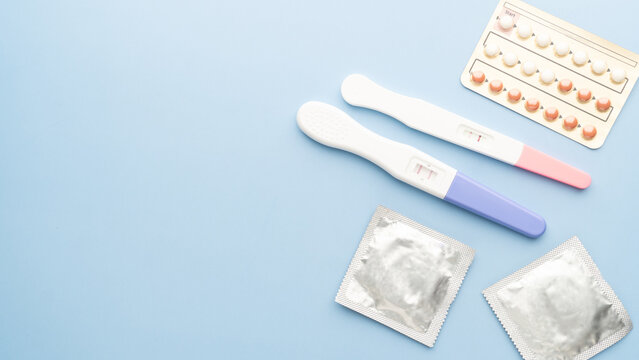 Pregnancy test with birth control pills and condoms on blue background. Contraception, family planning, sexual and reproductive health concept.