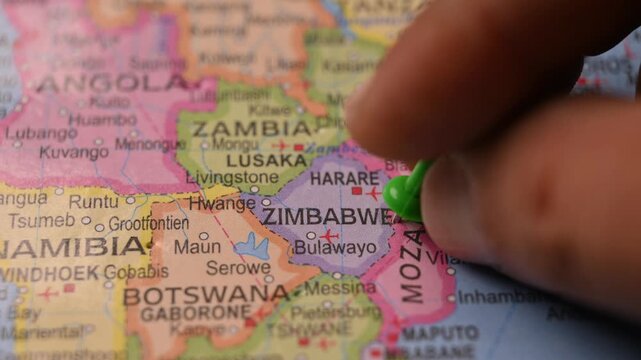 Travel Planning Scene with Hand Placing Green Pin on Zimbabwe in World Atlas Map