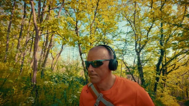 A modern mature man in his 50s using wireless headphones and sunglasses while hiking. Intersection of technology, gadgets, and active outdoor lifestyle. 4k quality.
