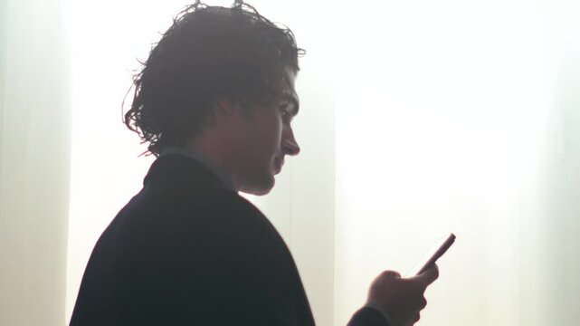 Man scrolling on smartphone in soft backlit window scene
