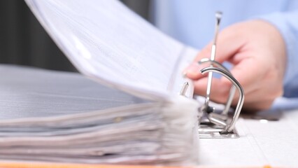Hand flipping through paperwork in a ring binder on an office desk, organizing business files and documents for accounting, audit, contracts and administrative record keeping © Aliaksandr