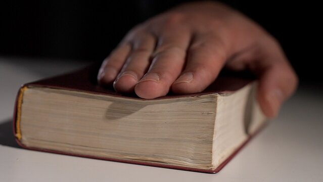 Person placing a hand on a holy book, symbolizing an oath, testimony, or witness statement in a judicial setting, emphasizing truth, justice, and legal integrity