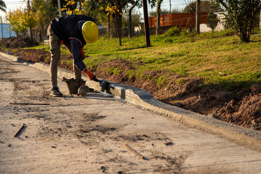 Construction worker finishing concrete curb with a brush and mortar on a new road