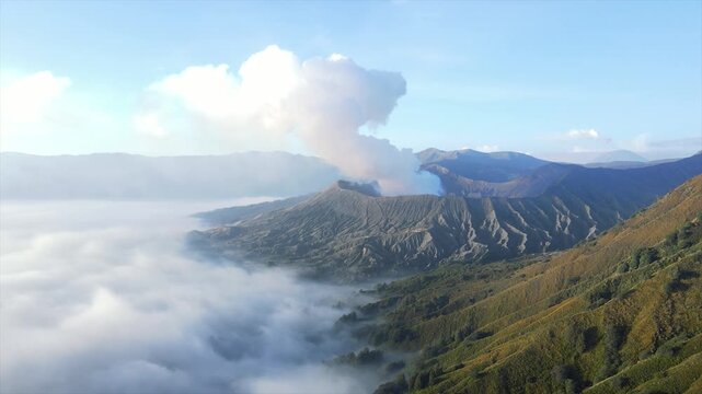 Stunning 4K wide shot of Mount Bromo volcano erupting smoke above a thick sea of clouds at dawn.