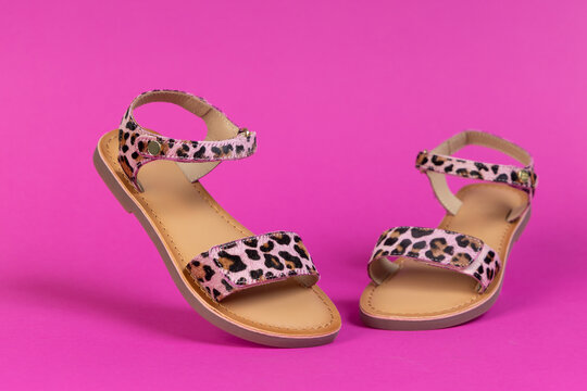 Stylish leopard print sandals with on pink background. Trendy summer footwear for women or girls. Fashionable flat shoes for vacation and casual wear.