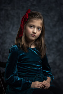 Fine art portrait of a little girl in a vintage green velvet dress. Timeless, painterly-style studio shot with a thoughtful, nostalgic mood.