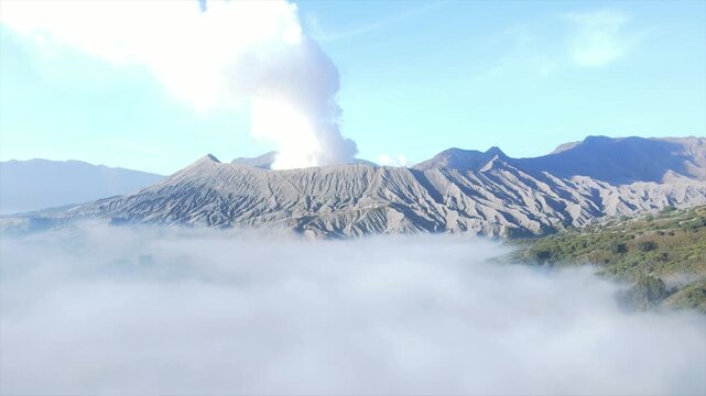Stunning 4K wide shot of Mount Bromo volcano erupting smoke above a thick sea of clouds at dawn.
