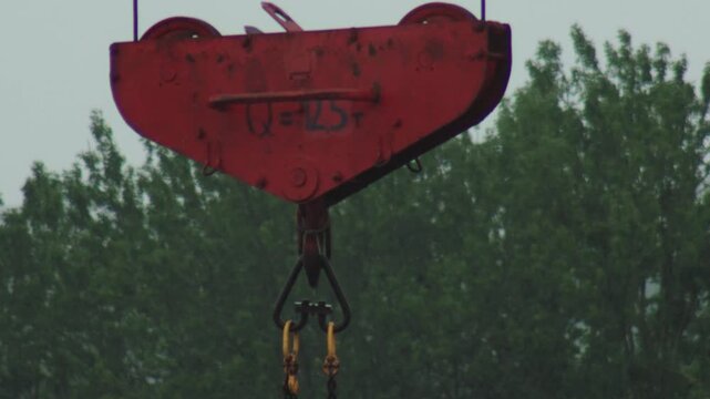 Weathered red crane hook block with Q equals 125 tons inscription. Industrial heavy lifting equipment, essential for large scale construction projects outdoors.