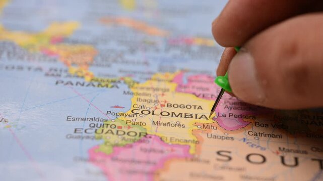 Man Pointing Green Pin at Colombia on Paper World Map