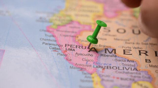 Man Pointing Green Pin at Peru on Paper World Map 
