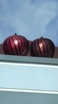 Close up view of two metallic, reddish-brown, spiraled ventilation system for residential or commercial property. Rotating roof turbines vent warm air from building structure under blue sky with fluff