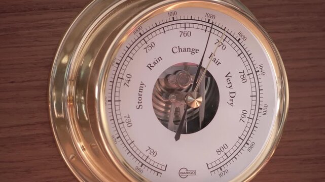 Circular brass barometer showing weather conditions from stormy to fair with scientific markings and metallic needle. Macro detail shot.