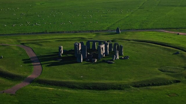 A sweeping aerial drone shot of the iconic Stonehenge monument located in Wiltshire, England. The massive ancient standing stones and circular earthworks are captured during low-sun hours.