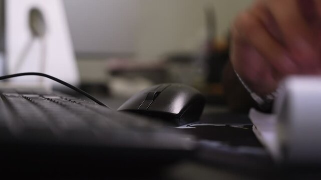 shot of a hand using a black computer mouse on a desk next to a keyboard. This indoor workspace scene highlights daily productivity and technology in a modern corporate office.