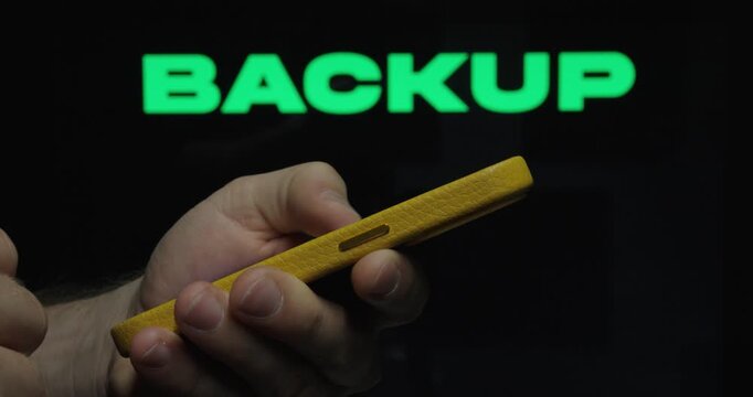 Close-up of a hand using a smartphone with &ldquo;Backup&rdquo; text, representing data protection, storage, and digital security.