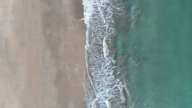4K Aerial top-down view: Waves breaking on sandy Enebrales beach in Punta Umbria, Spain.