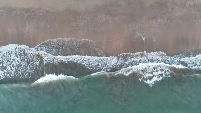 4K Aerial top-down view: Gentle waves crashing on sandy beach at sunset in Punta Umbria, Spain.