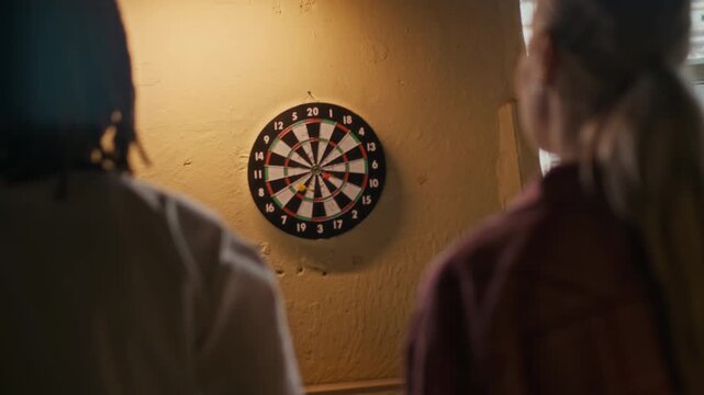 Rear view shot of young adult Black man throwing darts at dartboard then dapping female friend during casual competition at bar