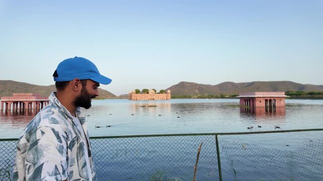 A young man wearing a blue cap looks towards Jal Mahal palace.
