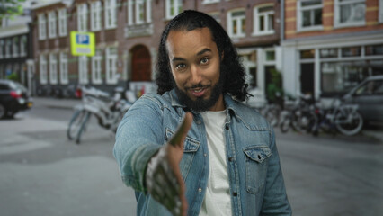 Fototapeta premium Man extends hand for handshake on street in city, denim jacket visible and bicycle row behind him; friendliness connection.