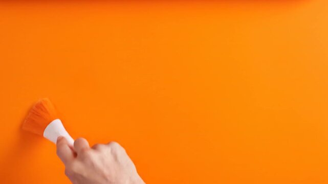 A hand wields a paintbrush with orange bristles against vivid orange, symbolizing creativity, cohesion, and monochrome minimalism&mdash;an emblem of artistic unity and expression.