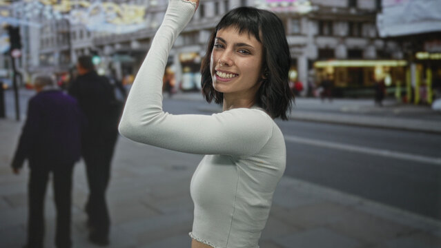 Woman raising her arm with a subtle smile in front of urban building facades on a busy street; confidence.