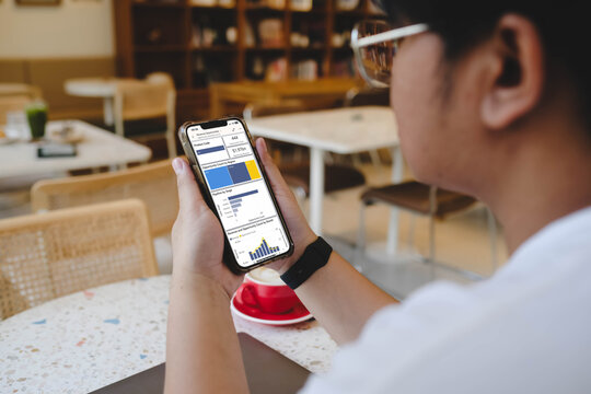 An unrecognizable person holding a smartphone that displays a generic business dashboard with financial revenue charts and sales pipeline statistics.
