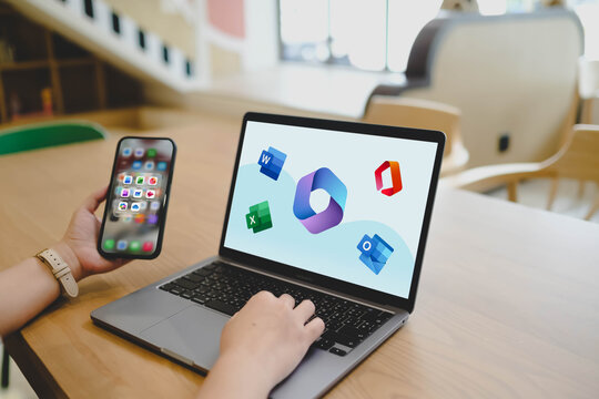 Bangkok, Thailand. April 30, 2026; A person uses a laptop and a smartphone to access Microsoft 365 productivity applications including Word, Excel, and Outlook while working in a bright workspace.