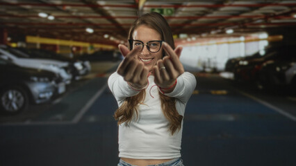 Fototapeta premium Woman wearing glasses and a white shirt making finger heart gesture with hands in parking building; playful affection.