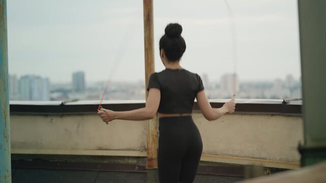 Young Black woman in activewear jumping rope alone on empty rooftop