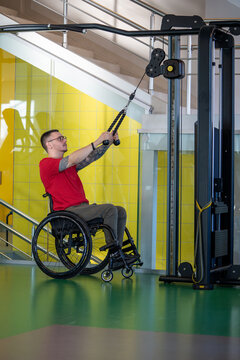 Determined strong man in wheelchair training arms and upper body on rehabilitation fitness machine for physical therapy, functional rehabilitation after trauma, adaptive strength training, male power