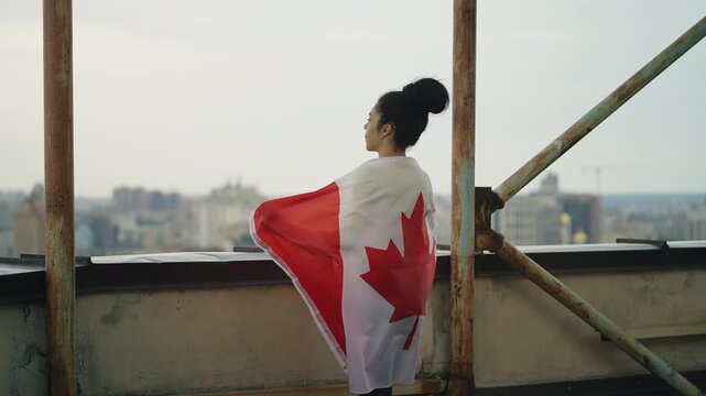 Happy Black woman holding Canadian flag on high rise rooftop, patriot